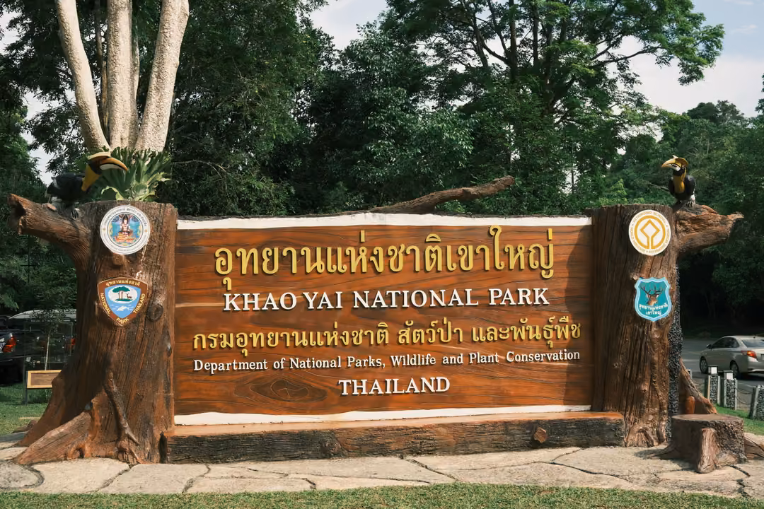 A wooden park entrance sign reading Khao Yai National Park in Thai and English, framed by trees