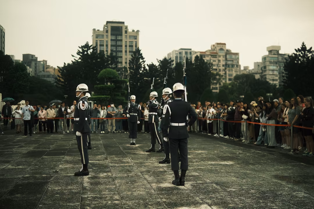 White-helmeted honour guards in dark uniforms stand on a wide plaza before a crowd behind red rope