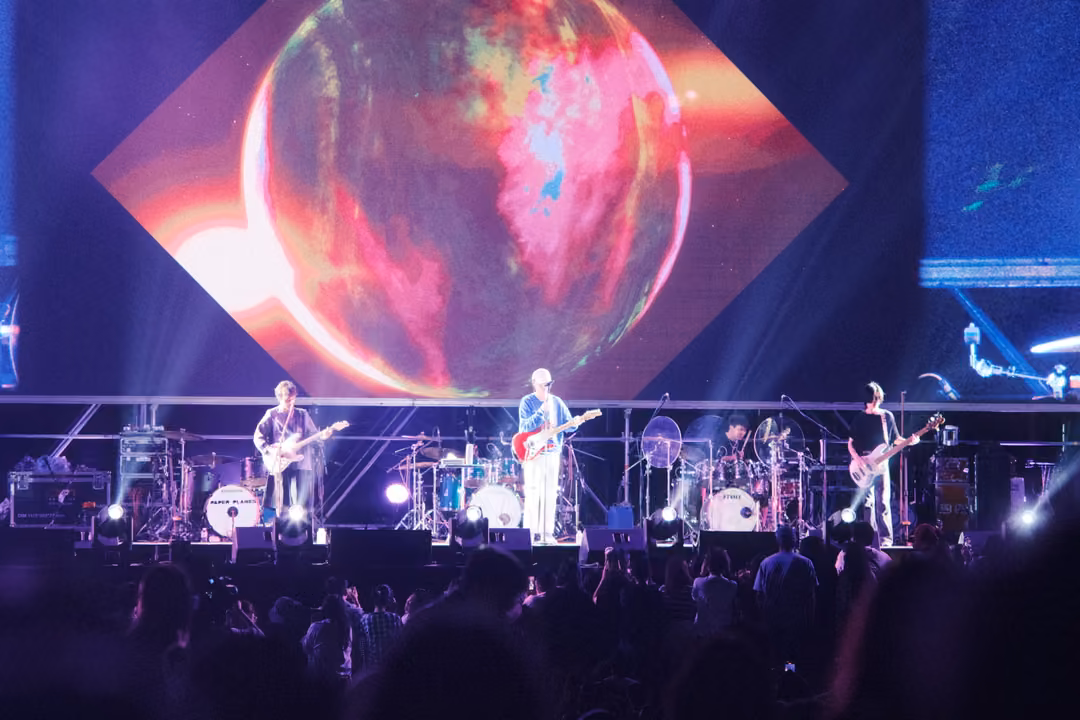 Band beneath a screen showing a glowing red and orange sphere framed by a diamond shape, crowd in the foreground.