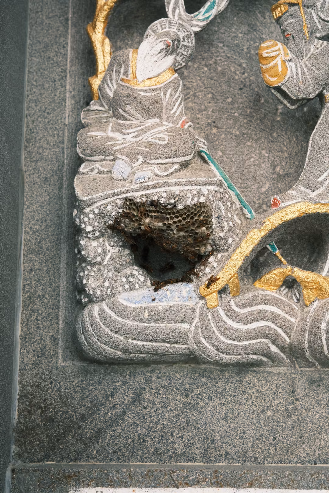 Close detail of a grey stone relief with painted gold accents and a small papery nest built into a hollow