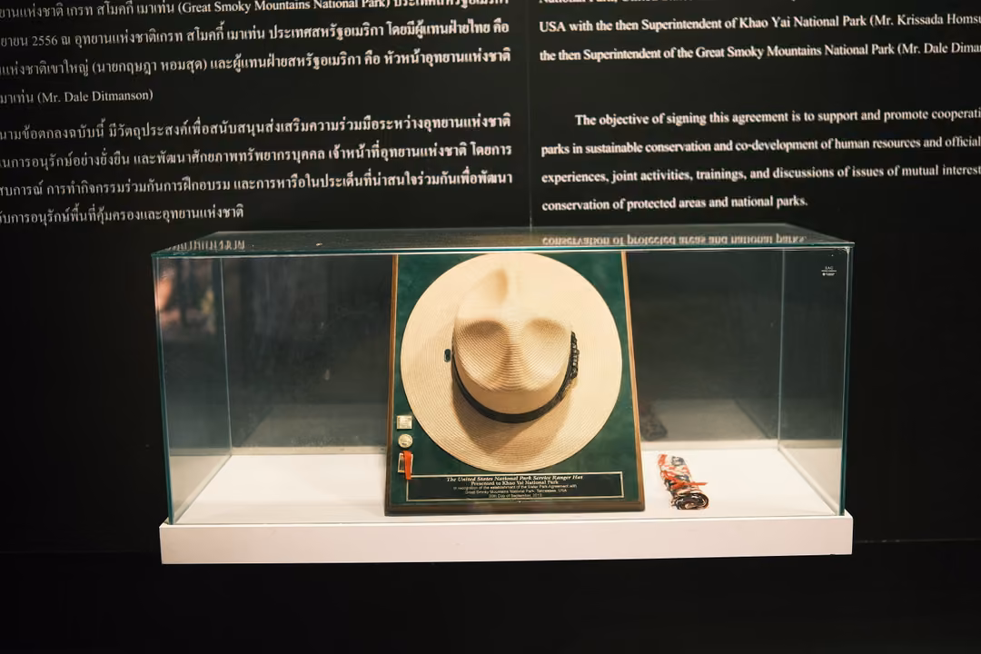 A brimmed ranger-style hat displayed in a glass case below a black panel of Thai and English text