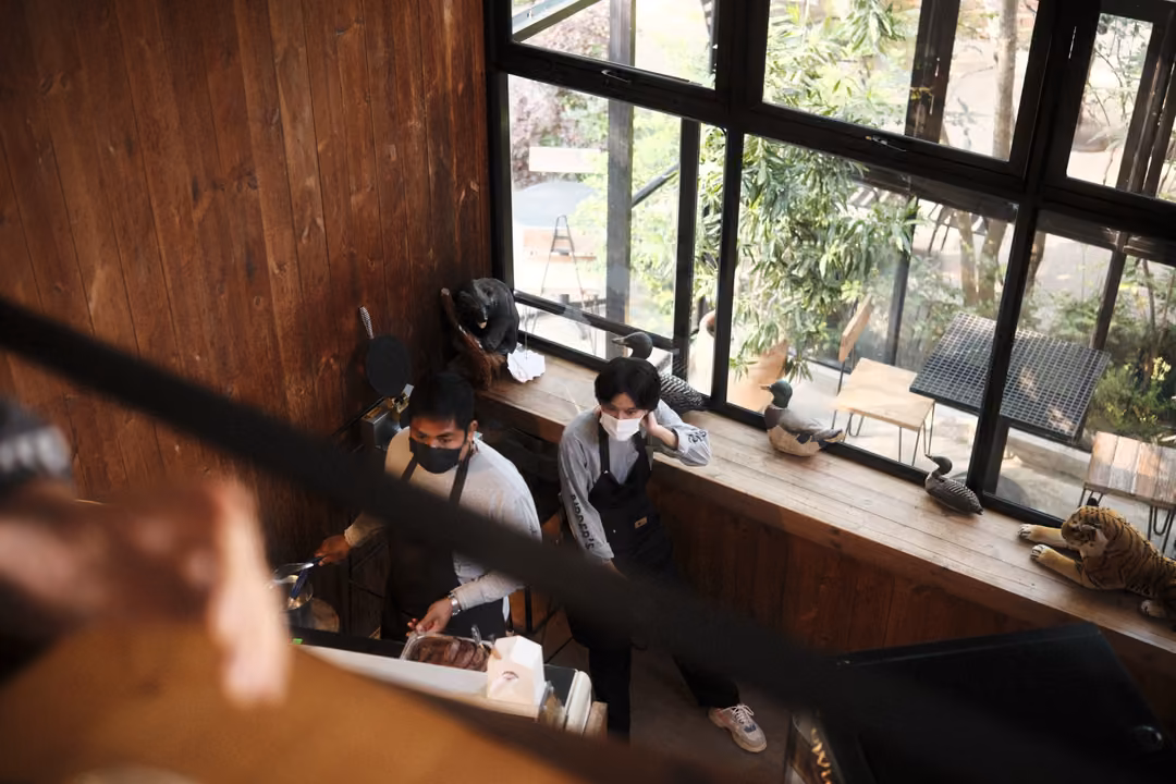 Looking down from above at two masked café staff working behind a counter by large windows