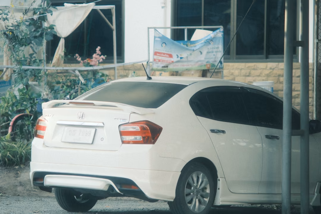 White sedan parked beside a building with a banner and plants, metal posts at right