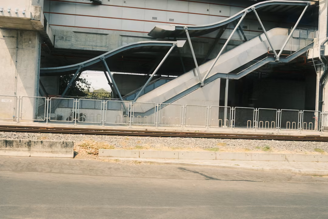 Elevated station stairway with curving metal canopies above railway tracks and a fenced platform