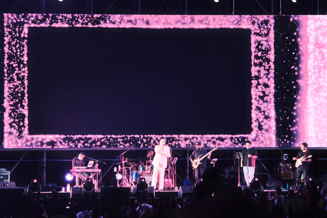 Pink glitter border around a dark screen, the band playing in purple light below