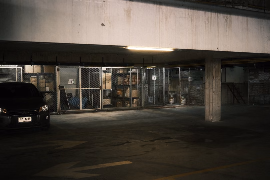 Dim underground car park with a parked dark car, a concrete pillar and caged storage areas
