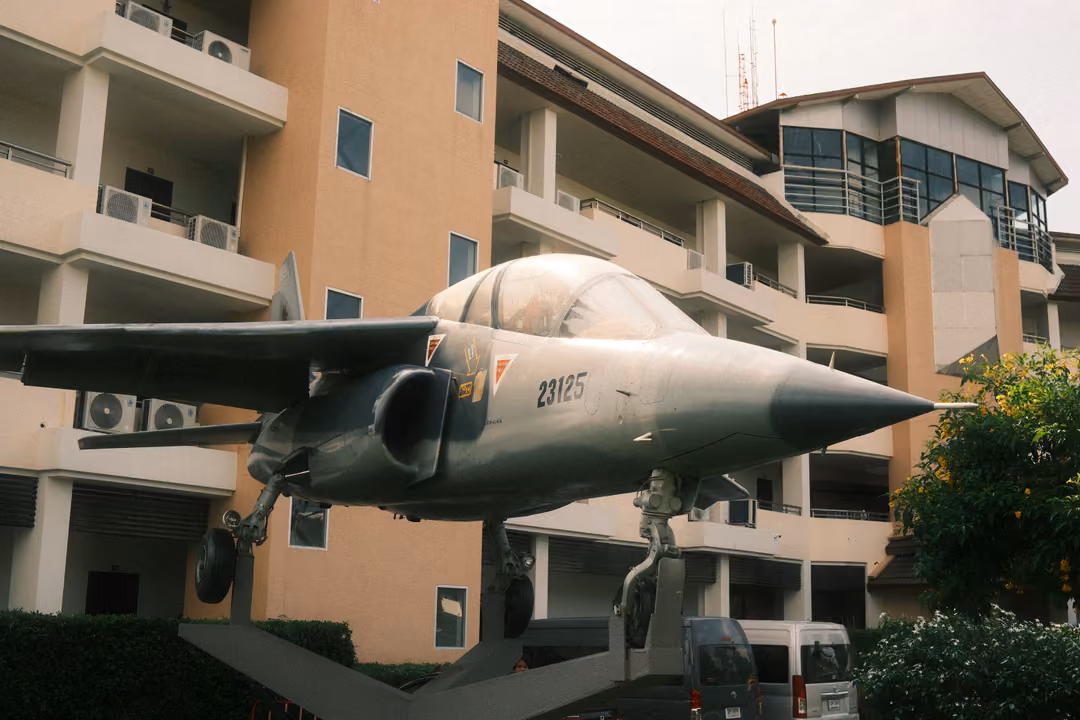 Side view of a grey jet fighter mounted on a pedestal, its pointed nose aimed across the frame toward trees
