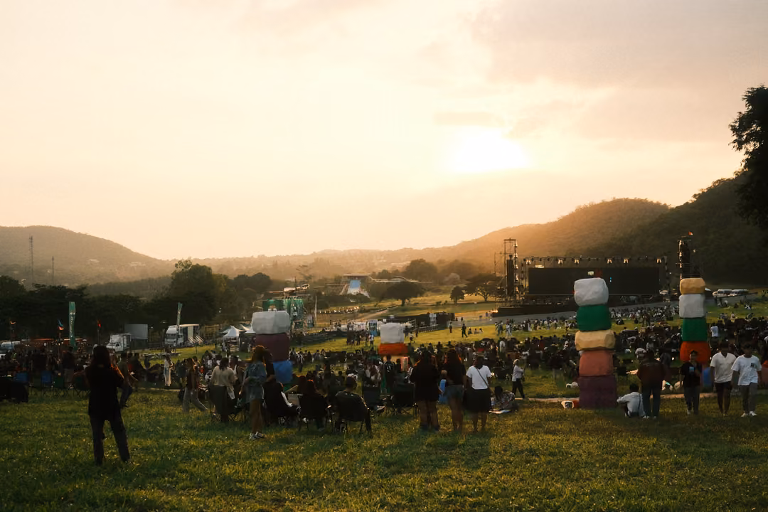 A crowd on a grassy hillside at sunset, stacked colourful cube towers and a distant stage.