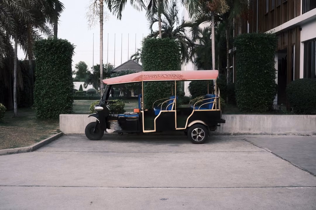 The same pink-canopied tuk-tuk parked before clipped hedges and palms, framed slightly wider