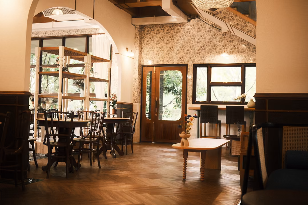 Café interior with a cream arch, floral wallpaper, wooden tables and chairs and a herringbone wood floor