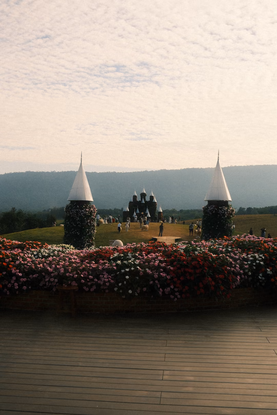 Upright view of the flower bed and twin cone towers framing the distant castle and mountains.