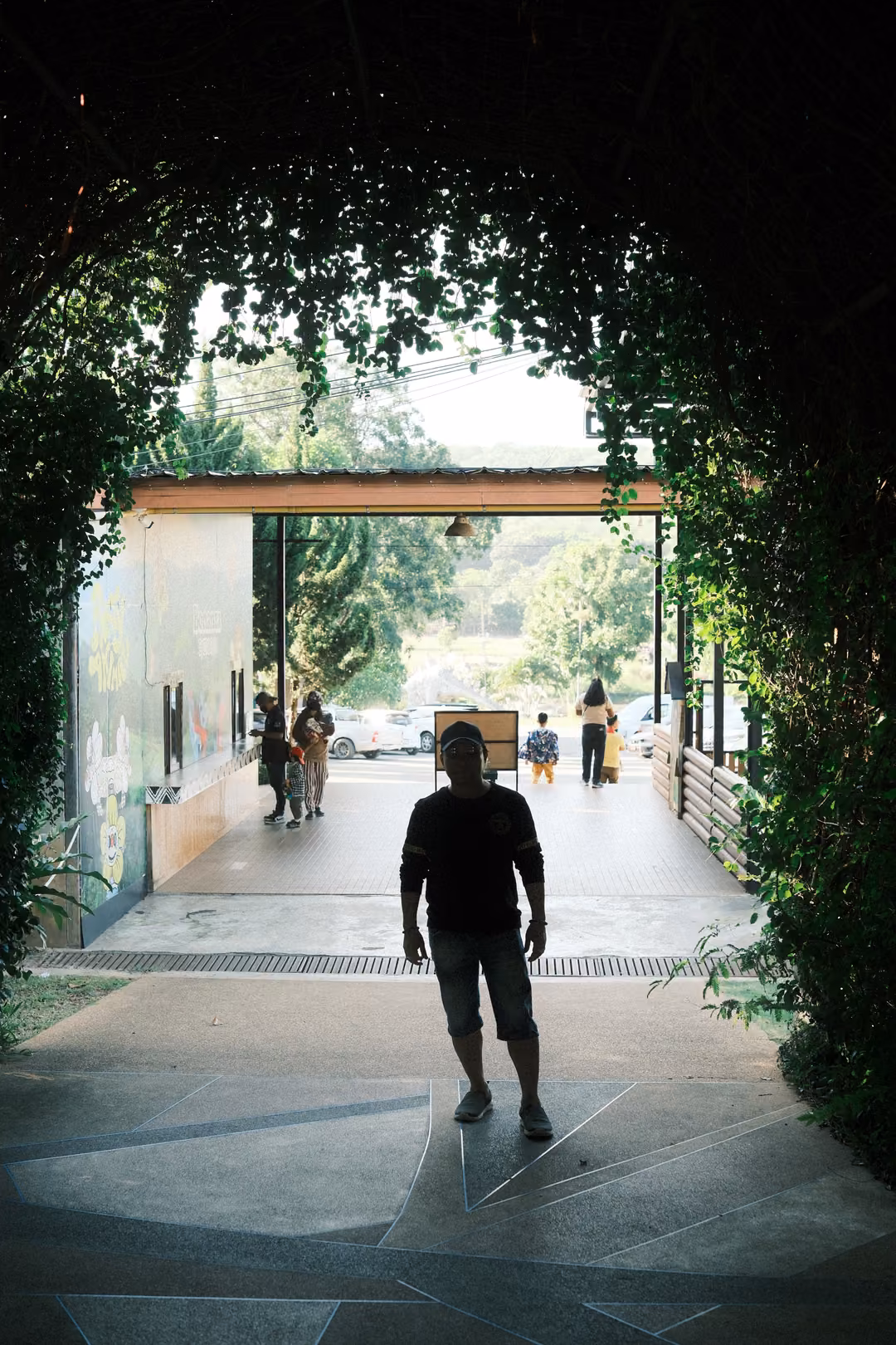 Silhouetted man walking toward camera through a vine-covered tunnel, bright entrance behind him