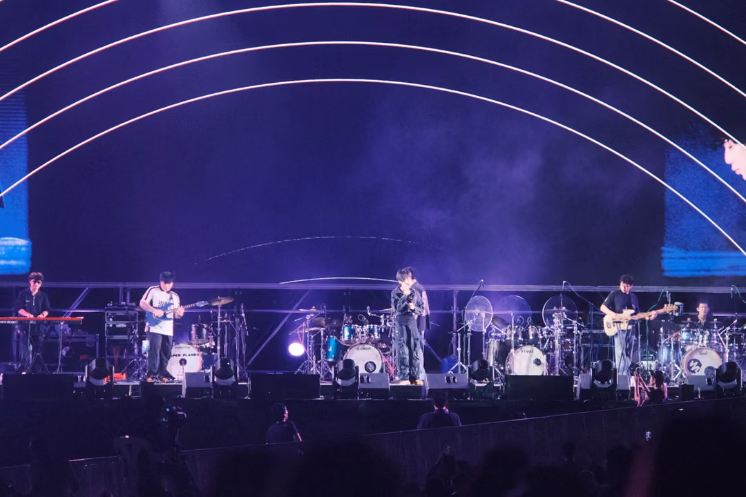 Band performing beneath a purple screen of concentric white arcs, smoke drifting across the stage.