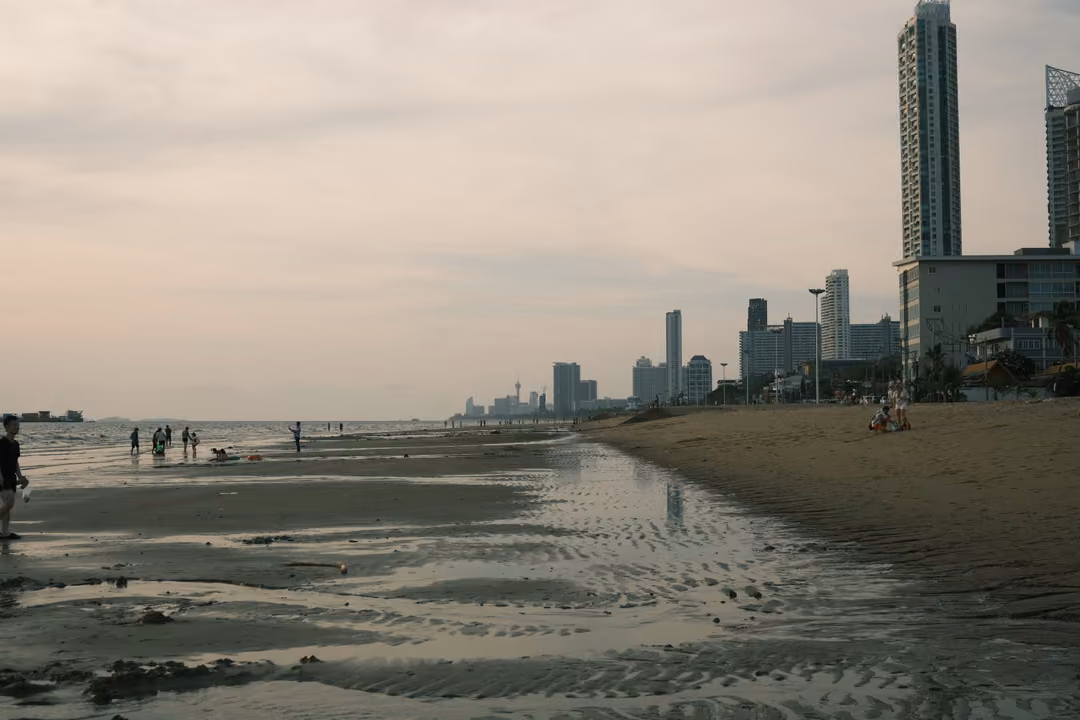 Wet, rippled sand reflecting the sky at low tide, people far off and towers along the shore