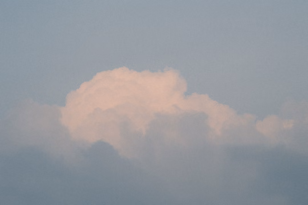 Rounded pink-tinted cloud above a layer of grey haze against a blue-grey sky