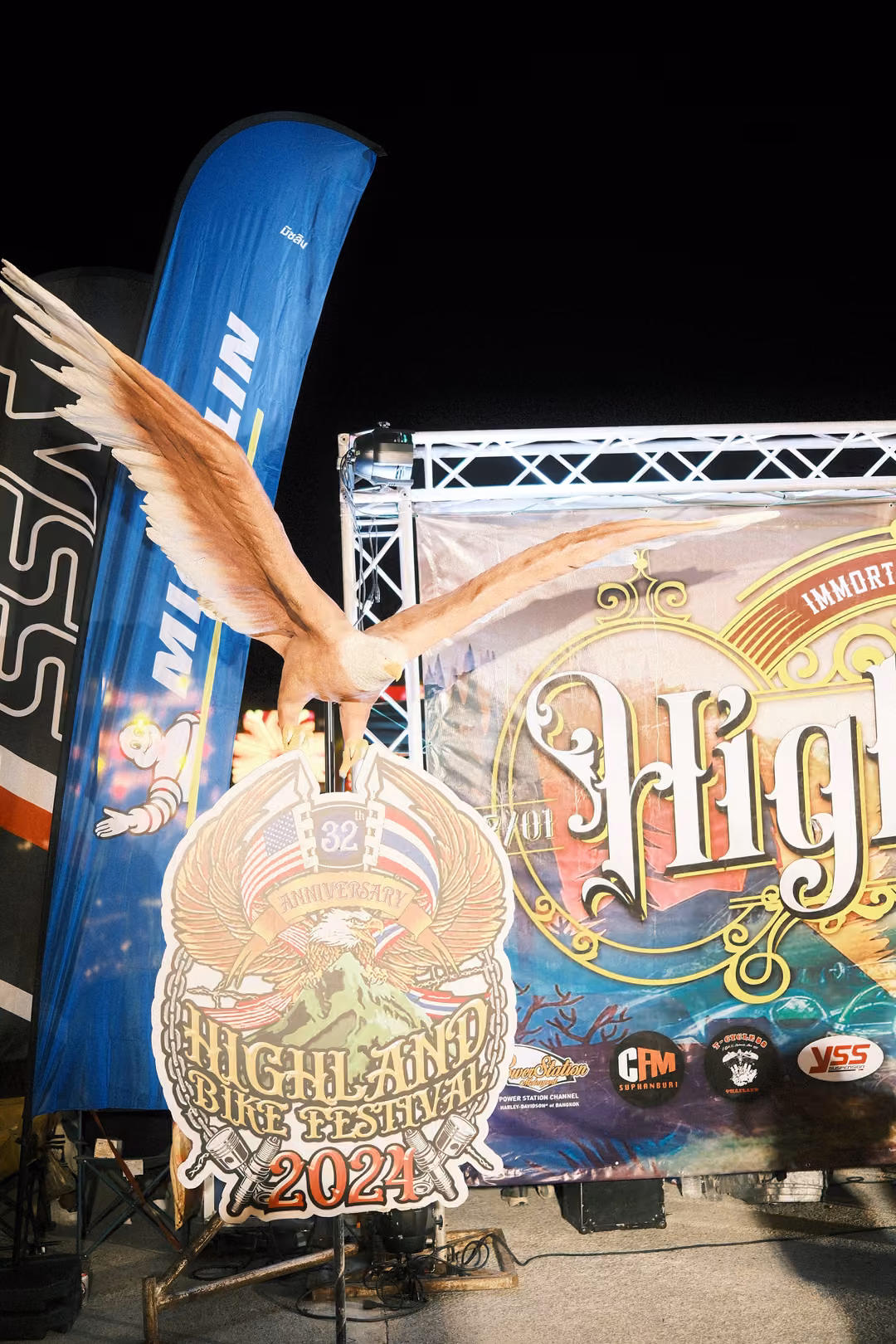 Carved eagle above a round Highland Bike Festival 2024 emblem in front of a decorative banner at night