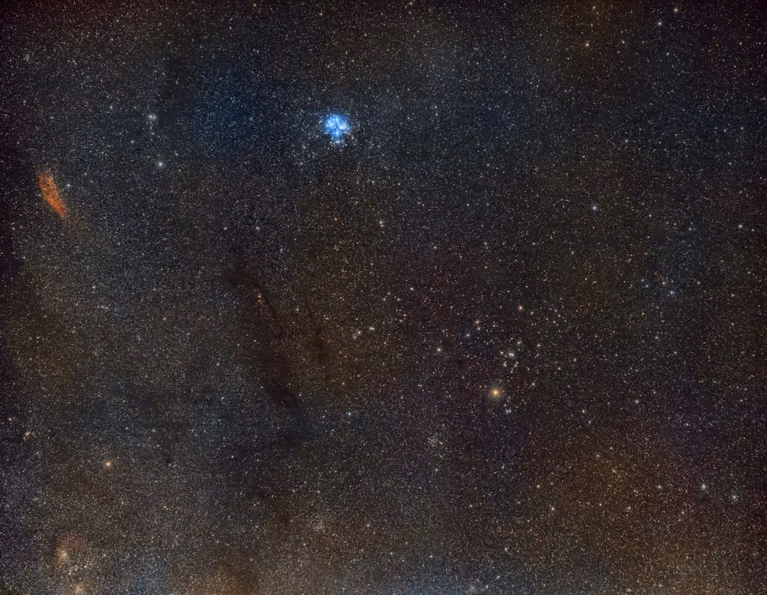 Starfield with a small blue star cluster, a red nebula at the left edge and dark dust lanes