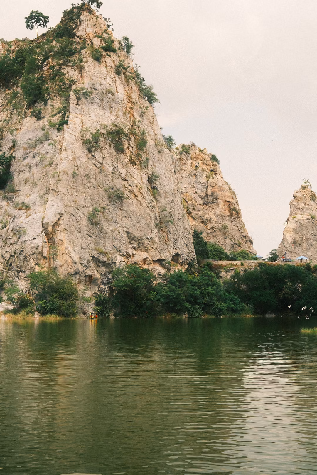 Pale limestone cliffs and a rock spire reflected in dark green lake water, vertical frame