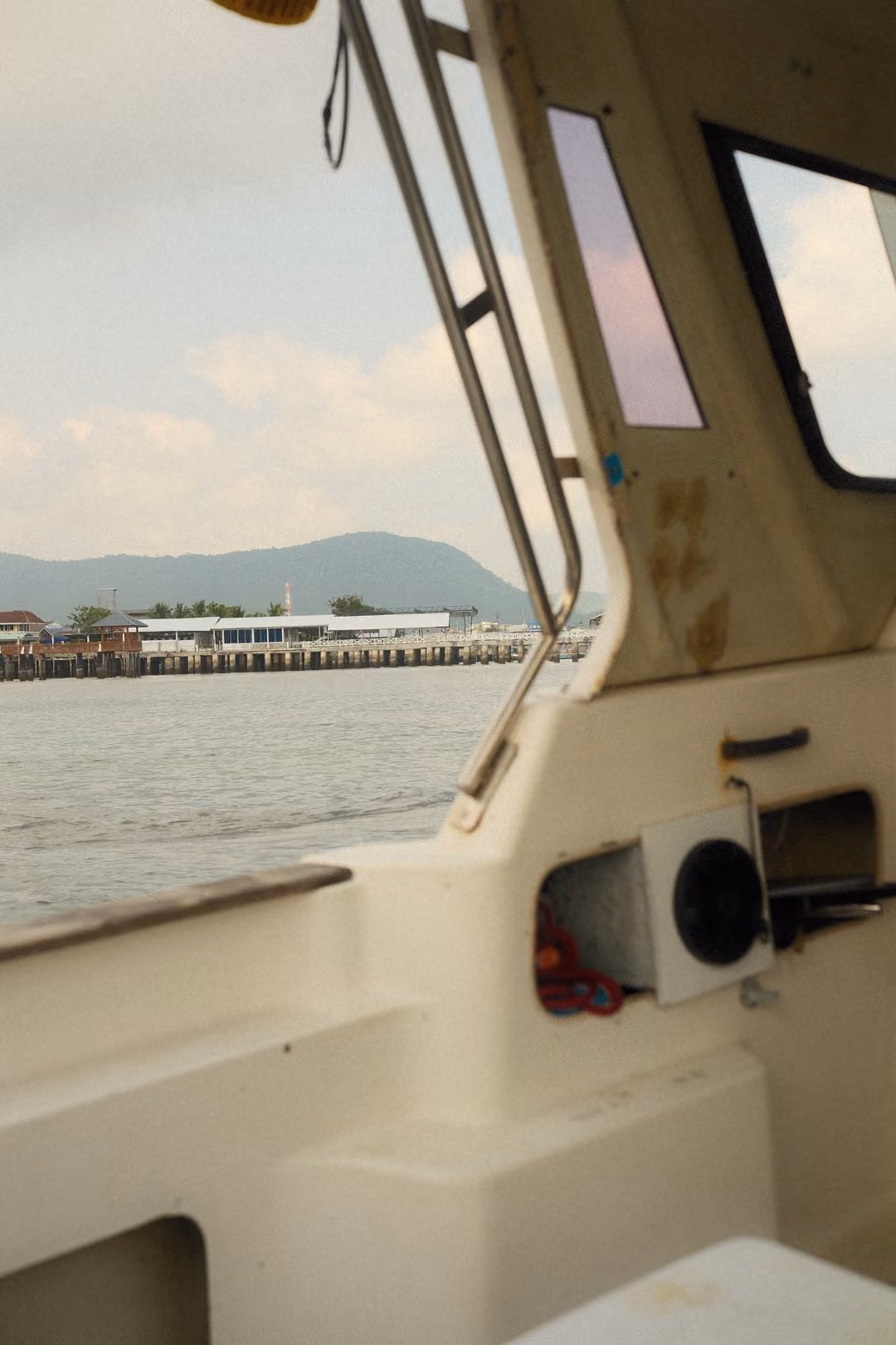 The pier and hill seen past the boat's side and handrail, with slightly more open sea in view.