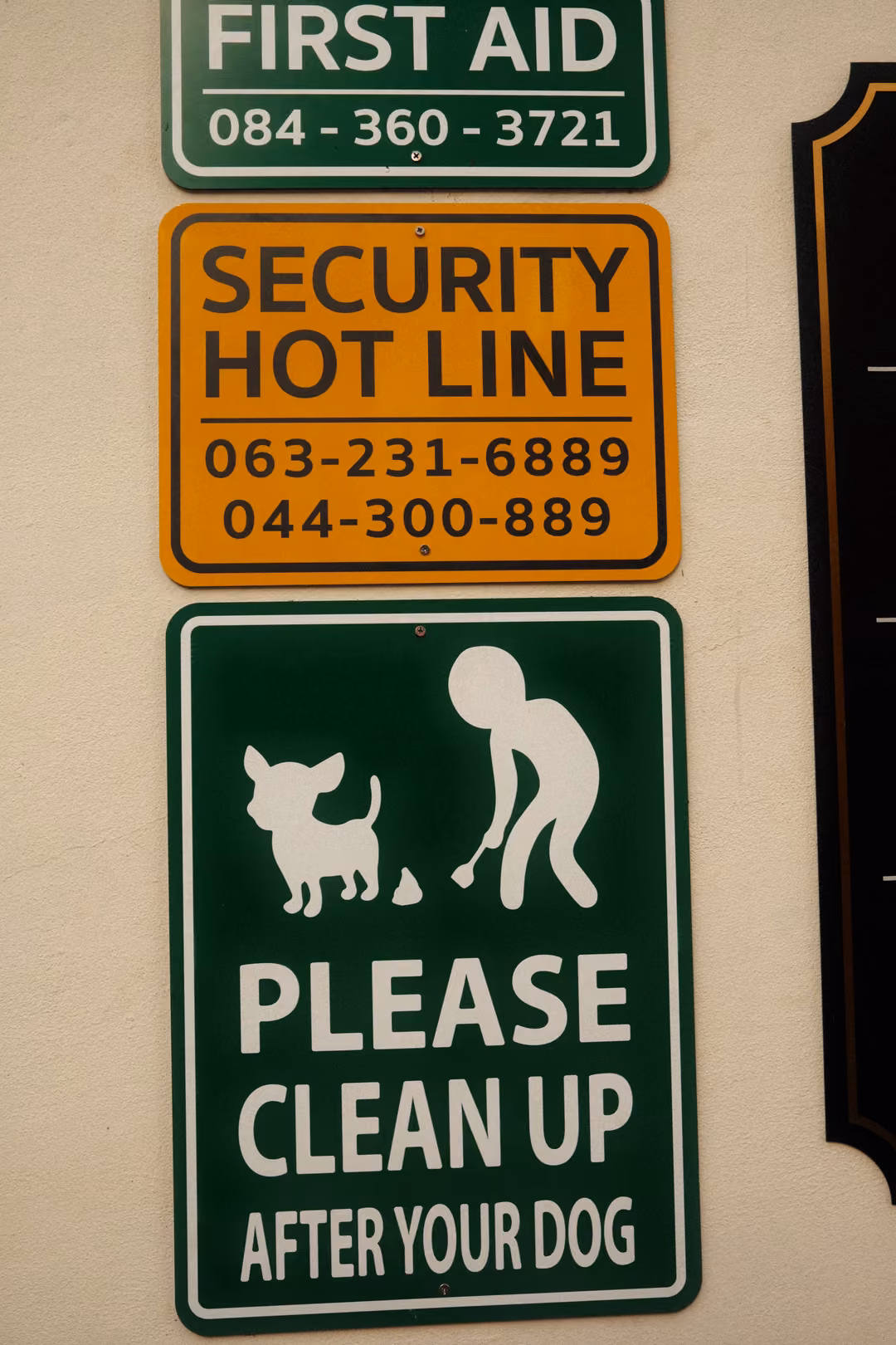 Three wall signs reading First Aid, Security Hot Line with phone numbers, and Please Clean Up After Your Dog