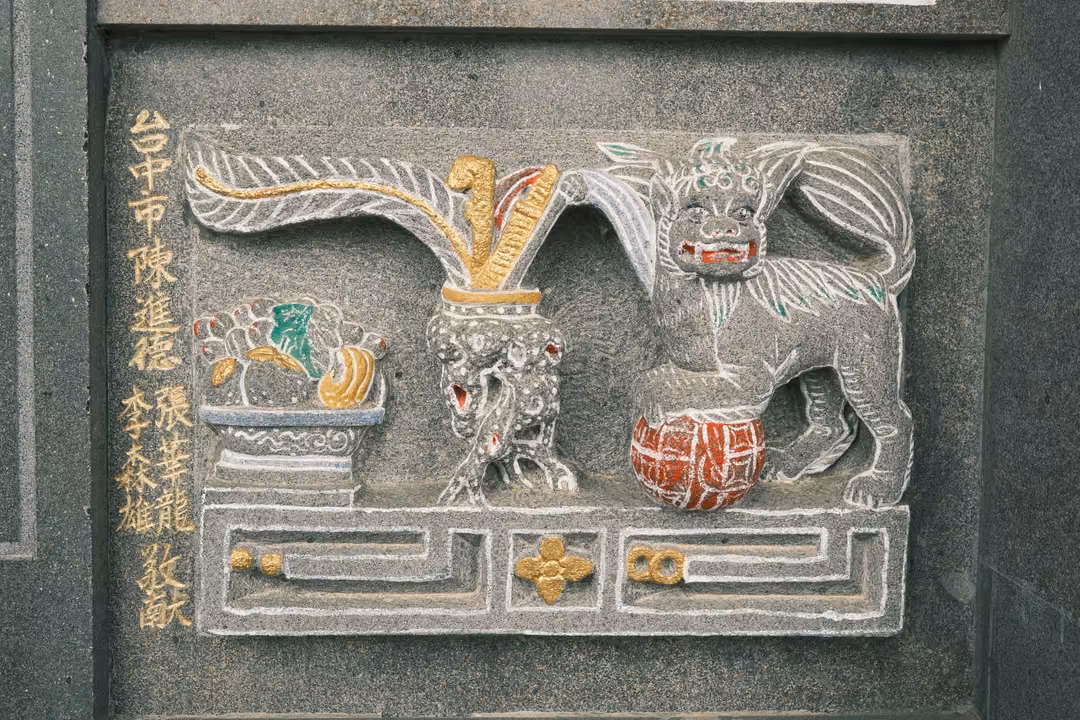 Stone relief of a guardian lion with a red ball beside a vase of feathers, gold-painted inscription at left