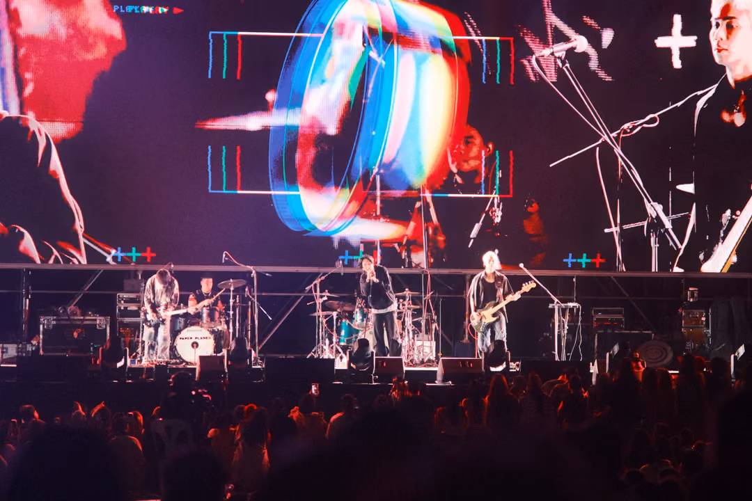 Band on stage below a screen showing a glowing ring with an RGB glitch effect, a guitarist close-up at right.