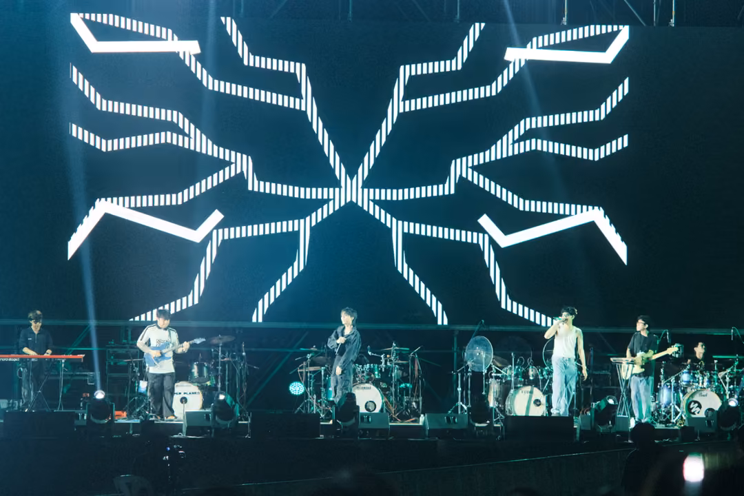 Stage with a screen showing a white dotted pattern of branching lines meeting in an X, band performing below.