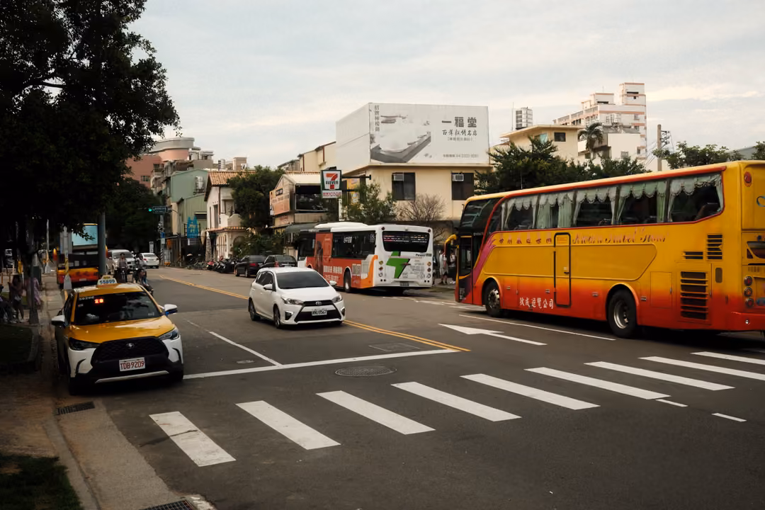 Street with a yellow and red coach bus, a taxi at the kerb, a white car and a pedestrian crossing