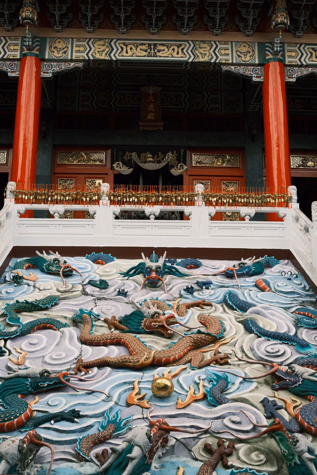 Painted dragon relief in blue and white clouds rising toward a temple hall with red pillars and gold eaves