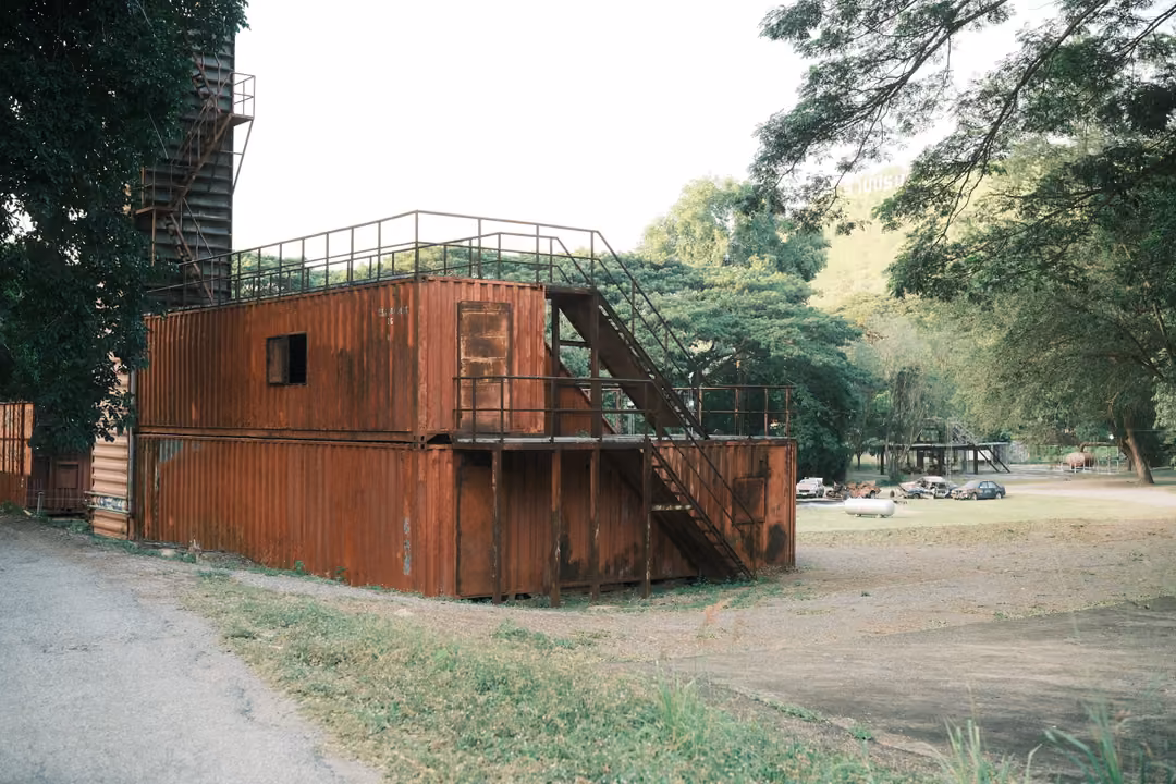 Two-storey structure built from rusty red shipping containers with external metal stairs and a rooftop rail