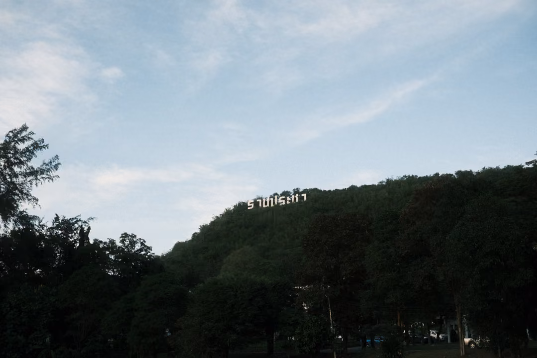 Blue sky with thin clouds above a dark forested hill with small white letters on its ridge
