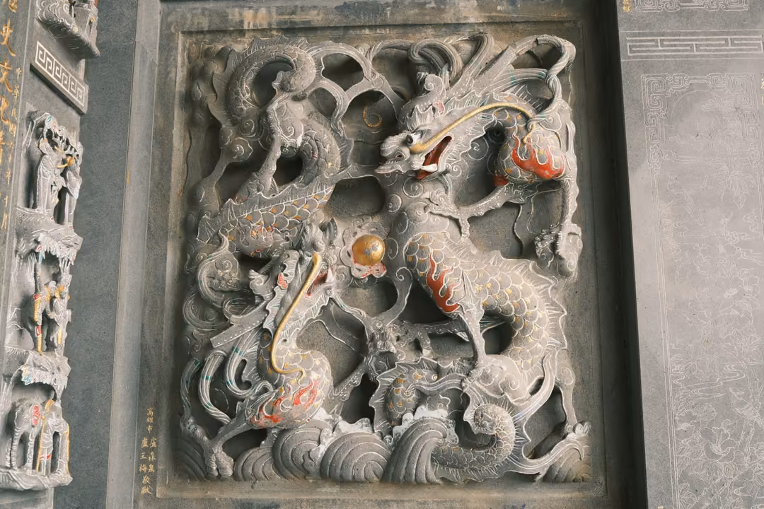 Deeply carved grey stone panel of dragons or qilin twisting among clouds and waves, flecked with red