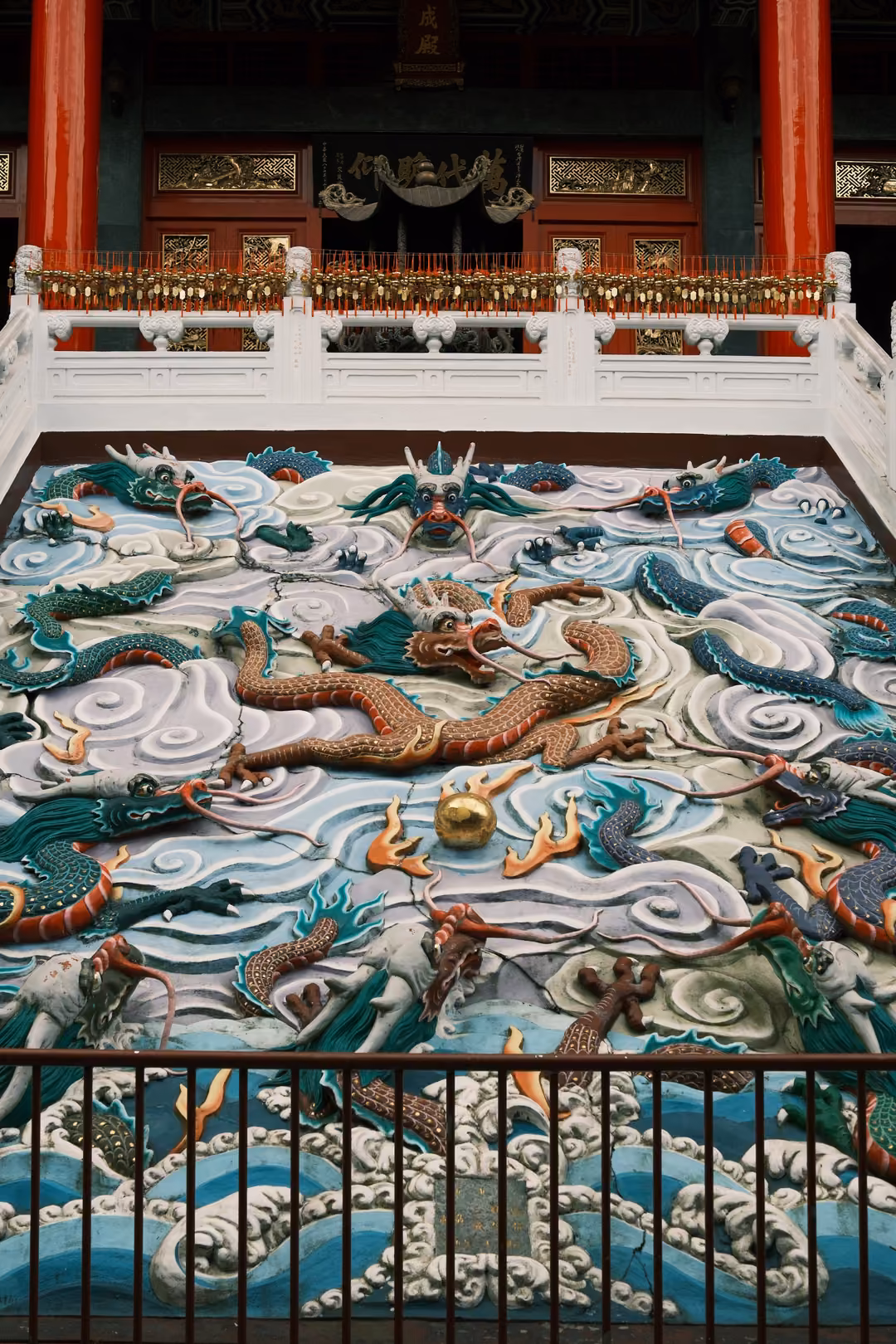 Brightly painted relief of dragons among white and blue clouds and waves below a temple balustrade and red pillars