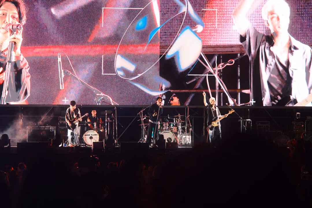 Screen showing the singer at a microphone, a spinning transparent ring and a guitarist close-up, band performing below.
