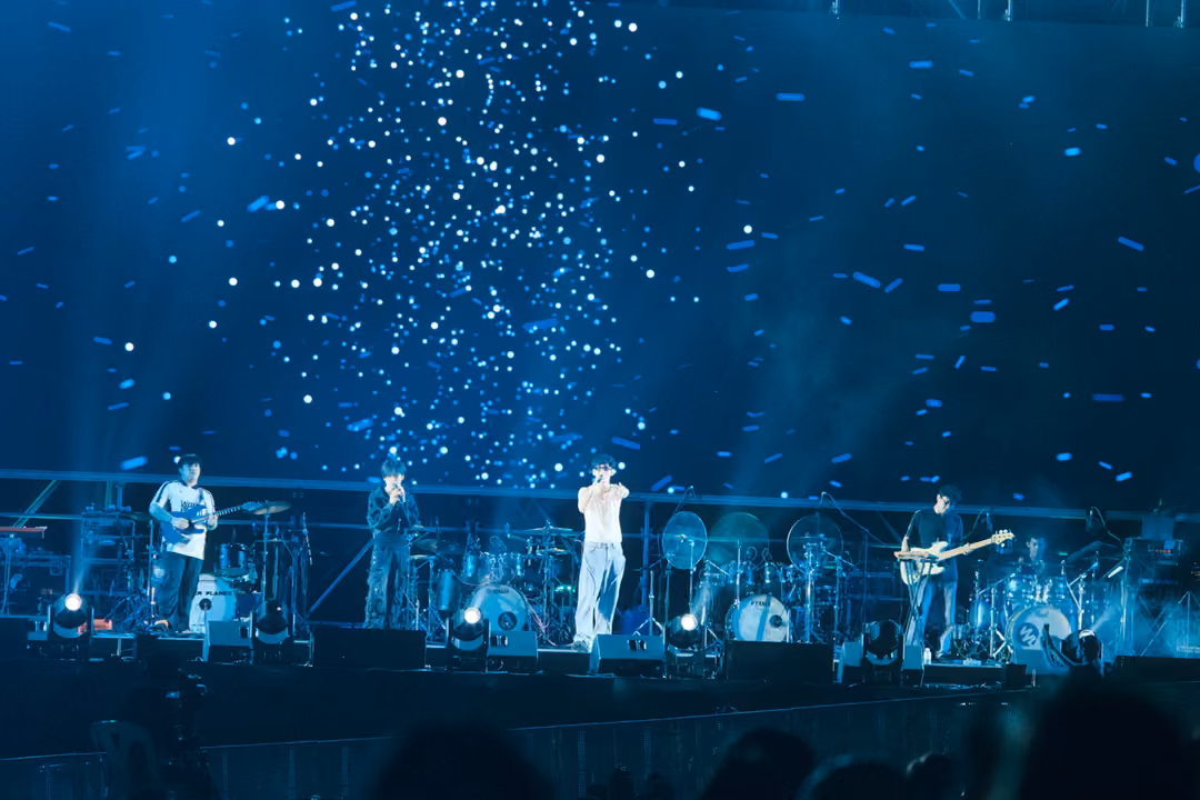 Band on a blue stage under a screen filled with drifting white specks like snow, lights glowing at their feet.