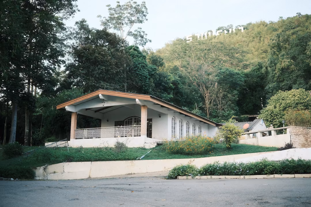 White pavilion with a peaked roof below a forested hill topped with white letters