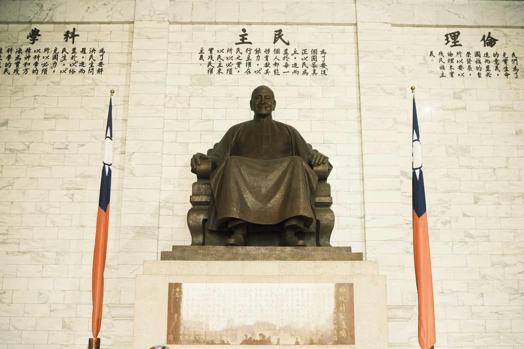 Bronze statue on throne between two flags, carved inscriptions above, warm evenly lit marble