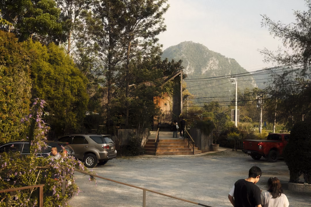 A paved courtyard with parked cars, steps and trees, a tall rocky hill rising behind