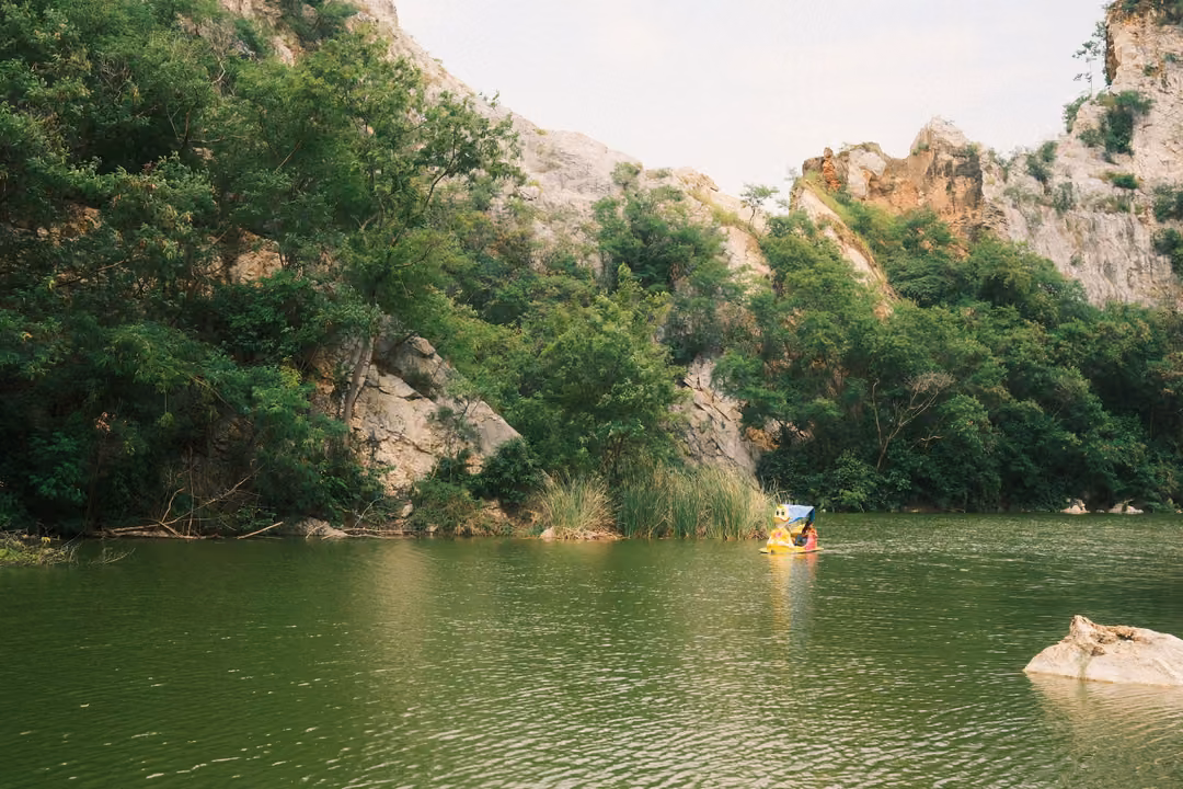 Green lake beneath tree-covered cliffs, a pale rock in the water and a small yellow pedal boat