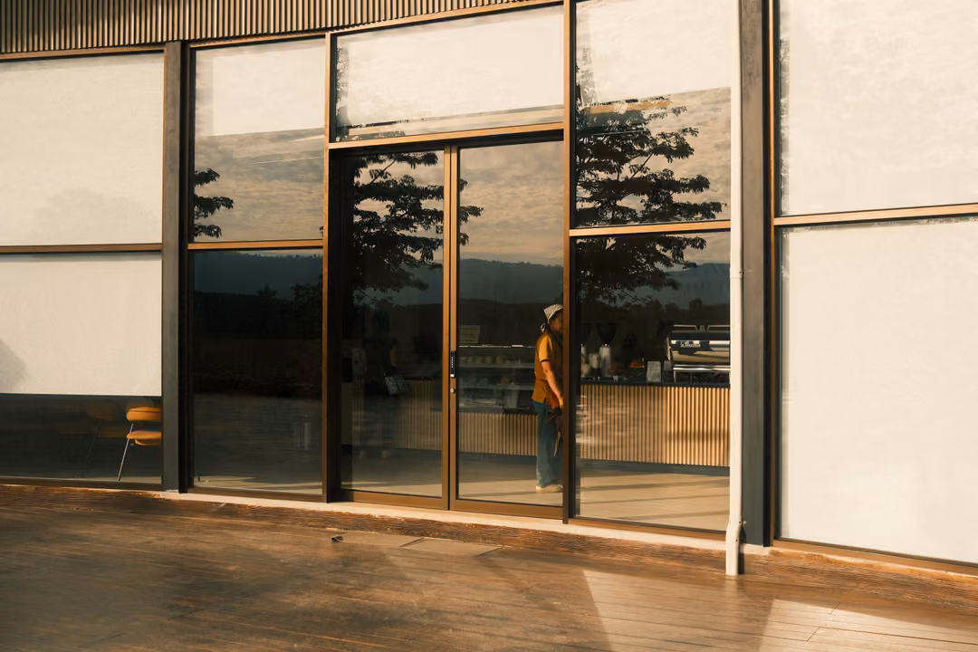 A glass café facade reflecting a tree and sky, a figure faintly visible through the door.