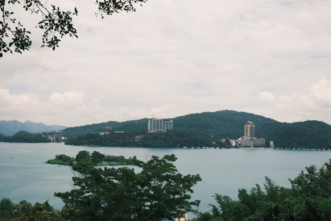 Lake viewed through overhanging leaves, a small island and hotel towers on a forested far shore
