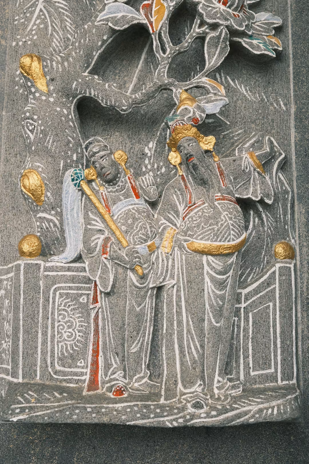Same stone relief of two robed figures beneath a blossoming tree, framed slightly lower and closer