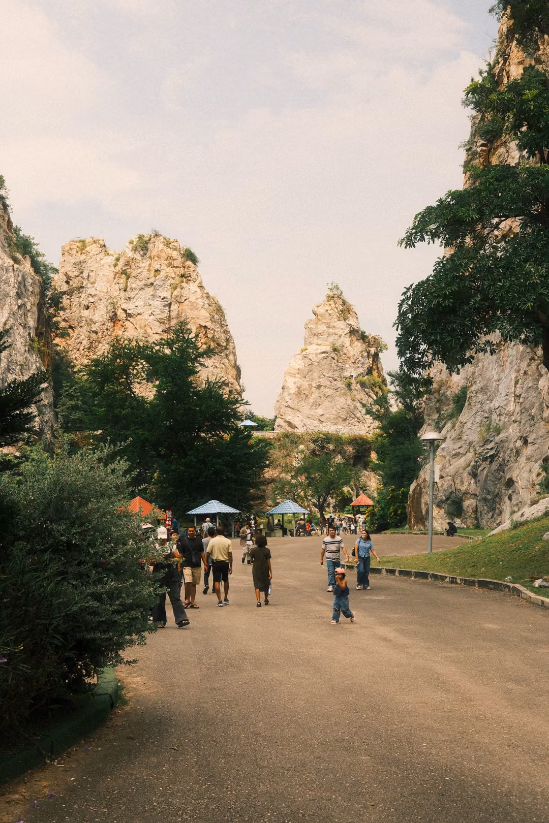 Road between rocky cliffs leading toward two pointed limestone spires, groups of visitors walking