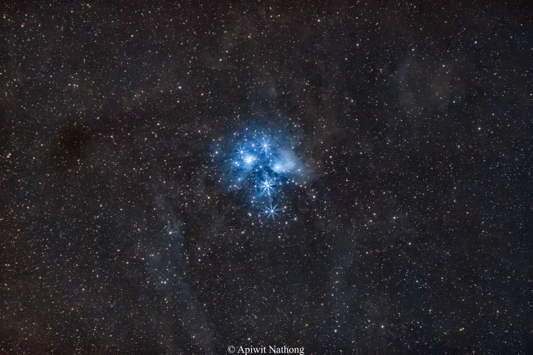 The Pleiades star cluster glowing blue with soft nebulosity, surrounded by dense faint stars and dust
