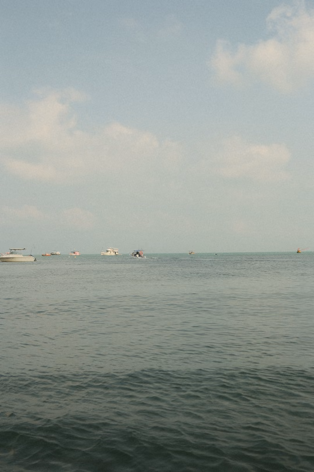 Calm grey-green sea stretching to the horizon, small white boats in the distance under light clouds.