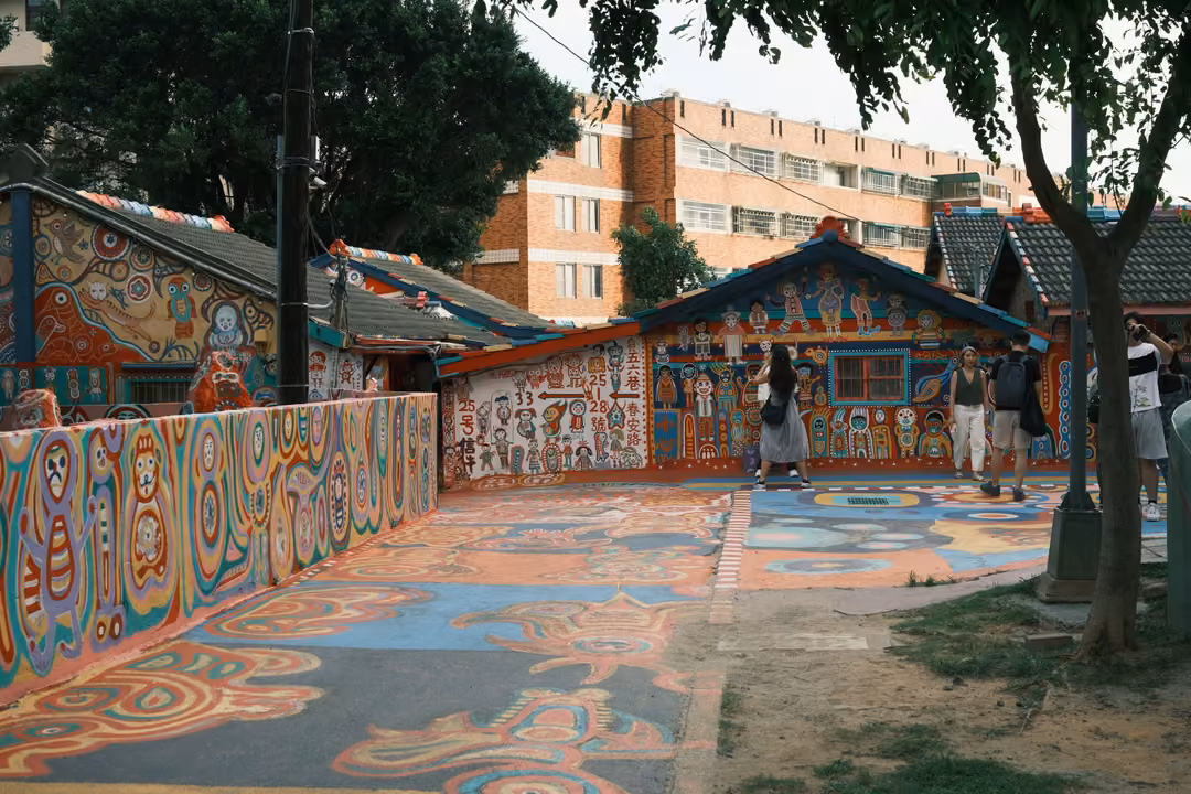 Low houses and walls covered in colourful painted patterns, painted courtyard ground, visitors walking
