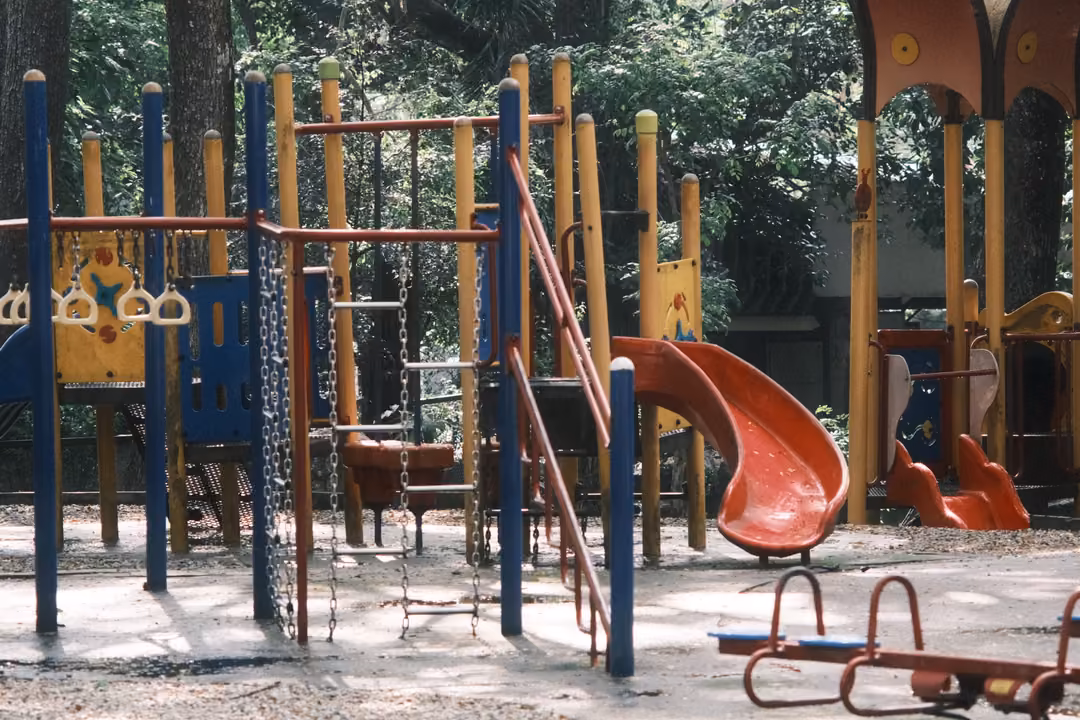 Playground climbing frame with blue and red poles, a red slide, hanging rings and a spring seesaw on sand