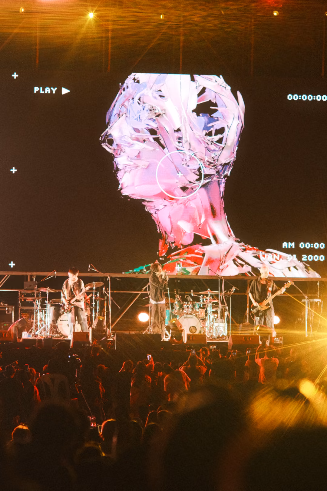 Vertical view of a screen showing a pink and white sculpted head with a PLAY label, warm amber lights flaring.